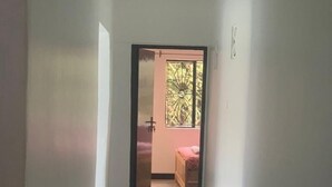 A narrow hallway with a tiled floor leading to a room with a bed and a window with a decorative metal grille. - Watu Guest House (Kampala)