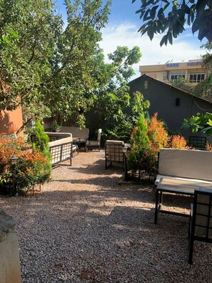An outdoor seating area with tables and benches, surrounded by gravel and greenery. - Watu Guest House (Kampala)