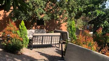 An outdoor seating area with a wooden table and two benches, surrounded by various plants and trees.