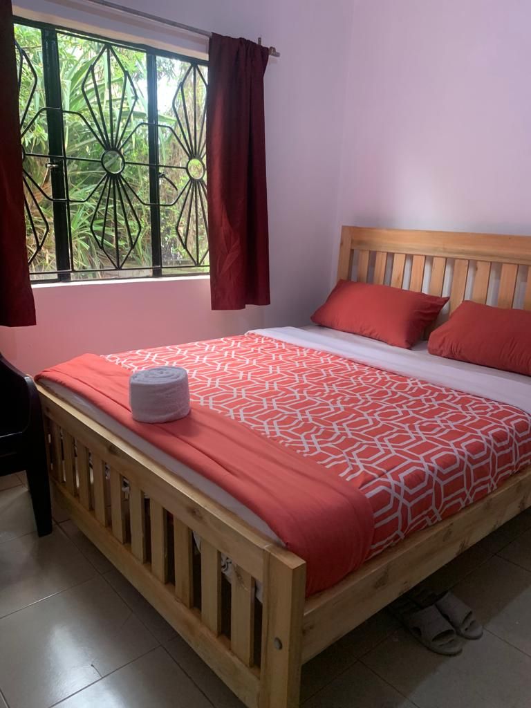 A single bed with a wooden headboard, a red patterned bedspread, and matching pillows.