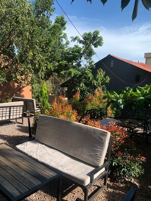 Un banco de madera con cojín en un jardín con diversas plantas y un edificio al fondo.