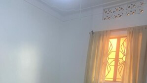 A room with a single bed, a window with curtains, and a white ceiling with a decorative panel. - Watu Guest House (Kampala)