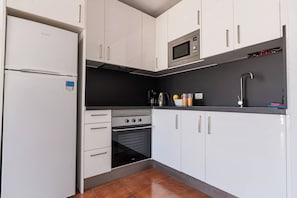 Una cocina compacta con gabinetes blancos, horno integrado, microondas y un lavamanos.
