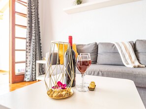 Una sala de estar moderna con un sofá blanco, una mesa de vidrio, una botella de vino y una copa de vino tinto.