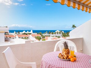 Uma varanda com mesa posta para o café da manhã, com vista para uma cidade costeira e o mar.