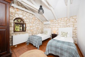 A bedroom with stone walls, two beds with checkered bedding, a wooden wardrobe, a radiator, and a hanging light fixture. - Villa Boscheto Tria - Three Bedroom Villa, Sleeps 6 (Ionian Islands)