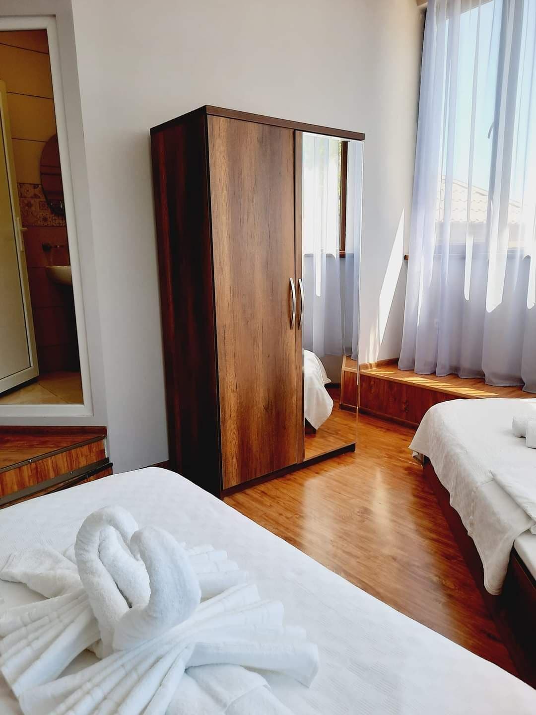 Una habitación de hotel con un armario de madera, dos camas con sábanas blancas y un espejo grande en la pared.