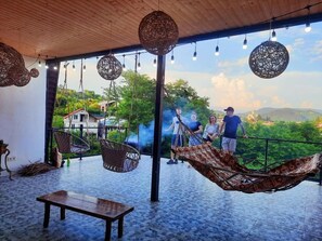 A spacious terrace with hanging wicker chairs, a wooden bench, and a view of a lush landscape. - Inaisi Hotel (Kutaisi)