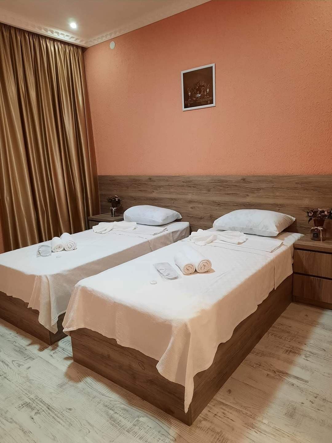 A hotel room with two beds, wooden headboards, a wooden floor, a beige wall, and a curtain.