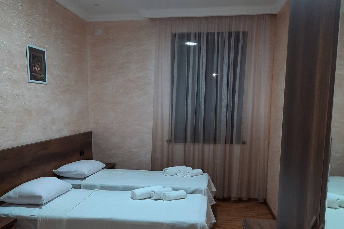 Une chambre d’hôtel avec deux lits, un plancher en bois, un luminaire au plafond et une fenêtre avec des rideaux.