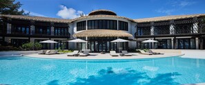 A resort with a large pool, multiple lounge areas, and a thatched-roof building.