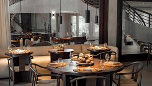 A modern dining area with round tables, cushioned seating, and a staircase in the background. - Villa Abrazos (San Pedro)