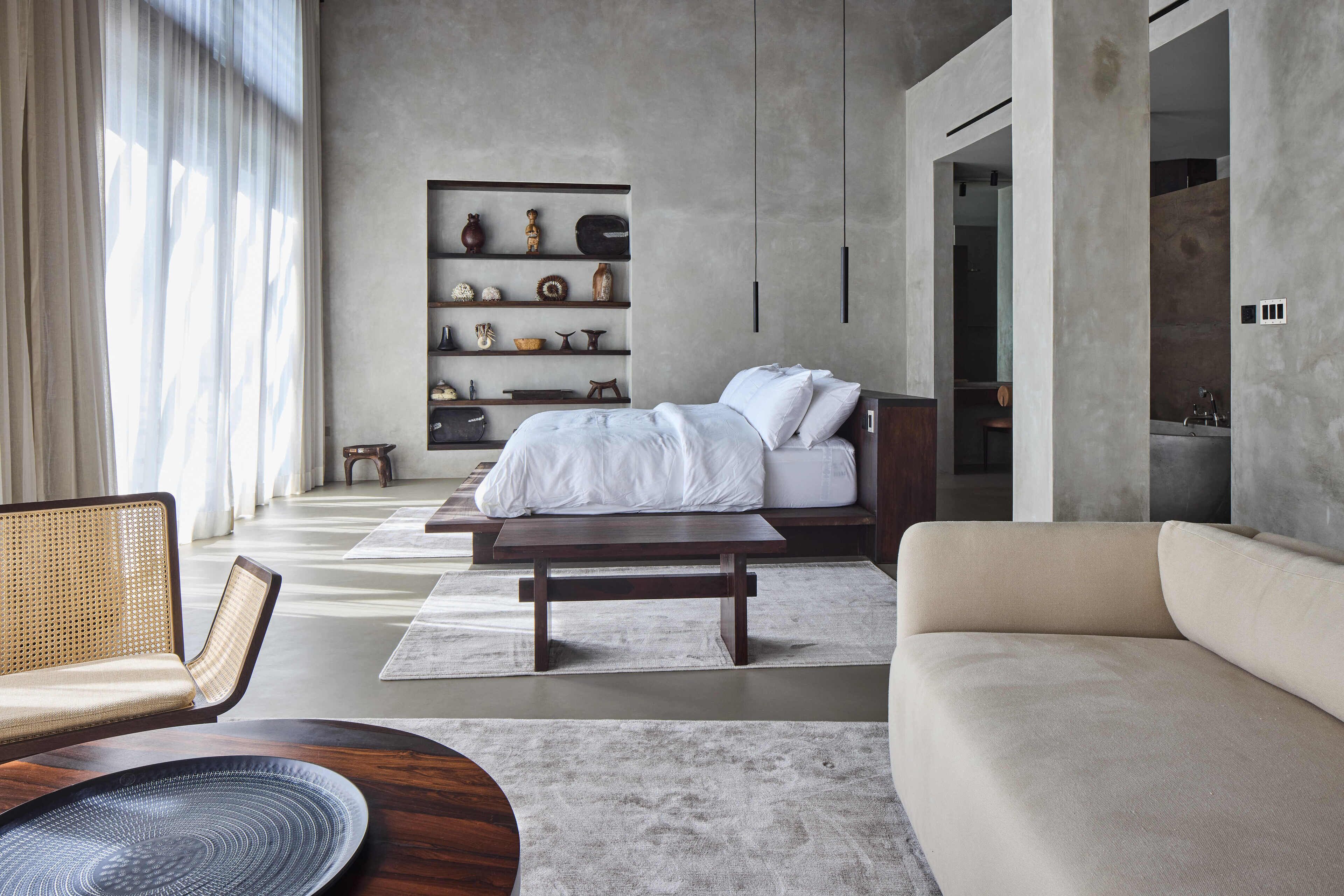 A modern bedroom with a large bed, a sofa, a wooden coffee table, and a bookshelf.