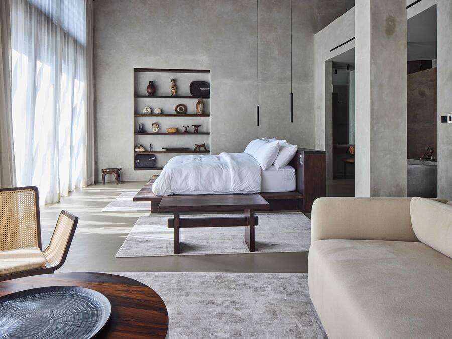 A modern bedroom with a large bed, a sofa, a wooden coffee table, and a bookshelf.