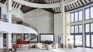 A spacious interior with a grand piano, modern seating, a spiral staircase, and large windows. - Villa Abrazos (San Pedro)