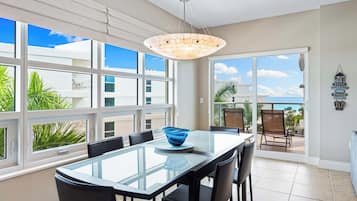 Un espace de restauration moderne avec une table et des chaises en verre, de grandes fenêtres et une vue sur l’océan.
