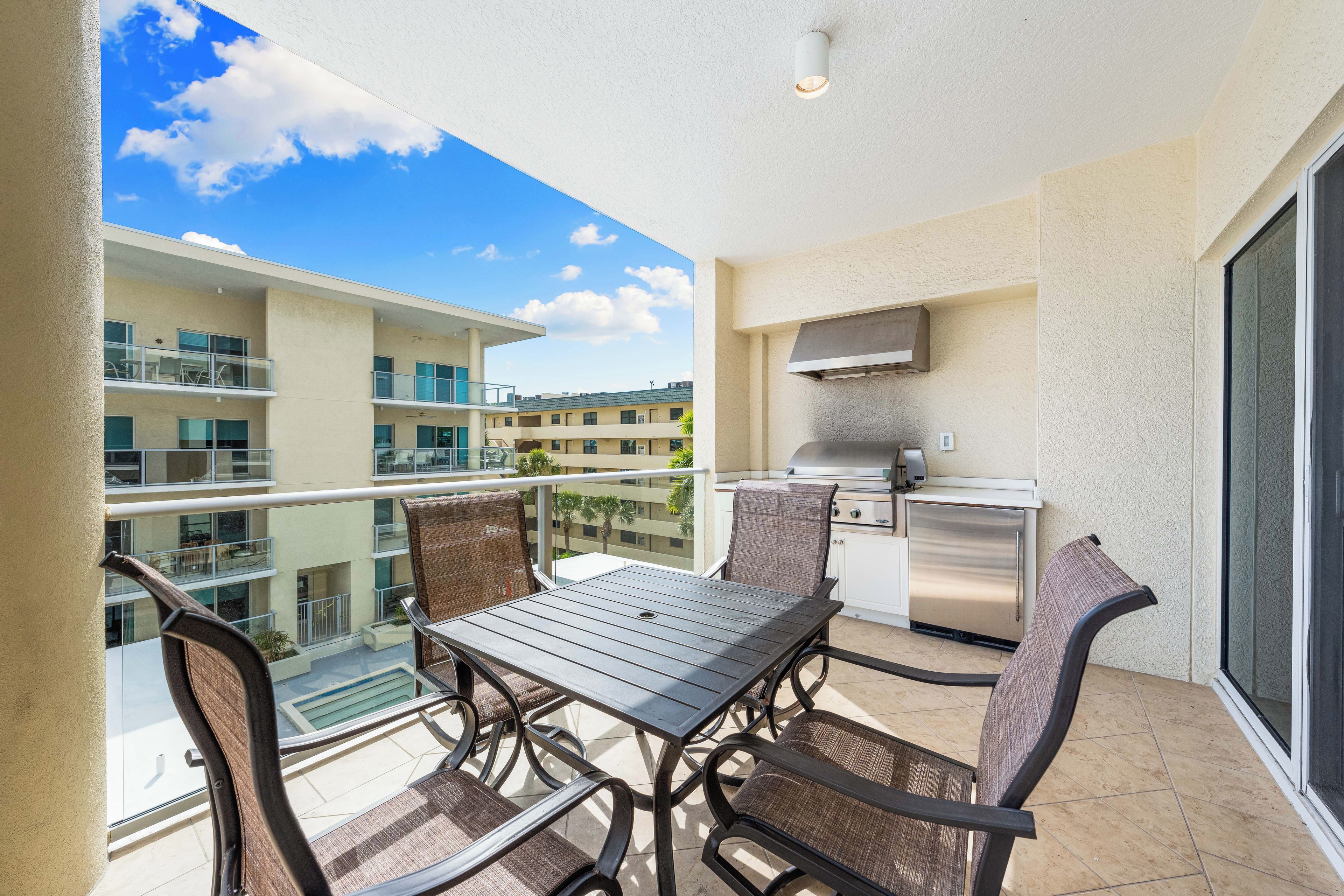 A balcony with a table and chairs, a grill, and a view of other buildings.