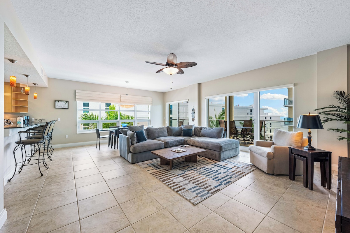 A spacious living room with a large sectional sofa, a coffee table, and a dining area with bar stools.