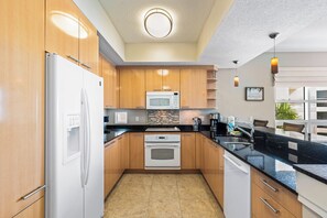 A modern kitchen with wooden cabinets, a white refrigerator, a microwave, and a built-in oven. - Crescent Condos by Beachside Management (Siesta Key)