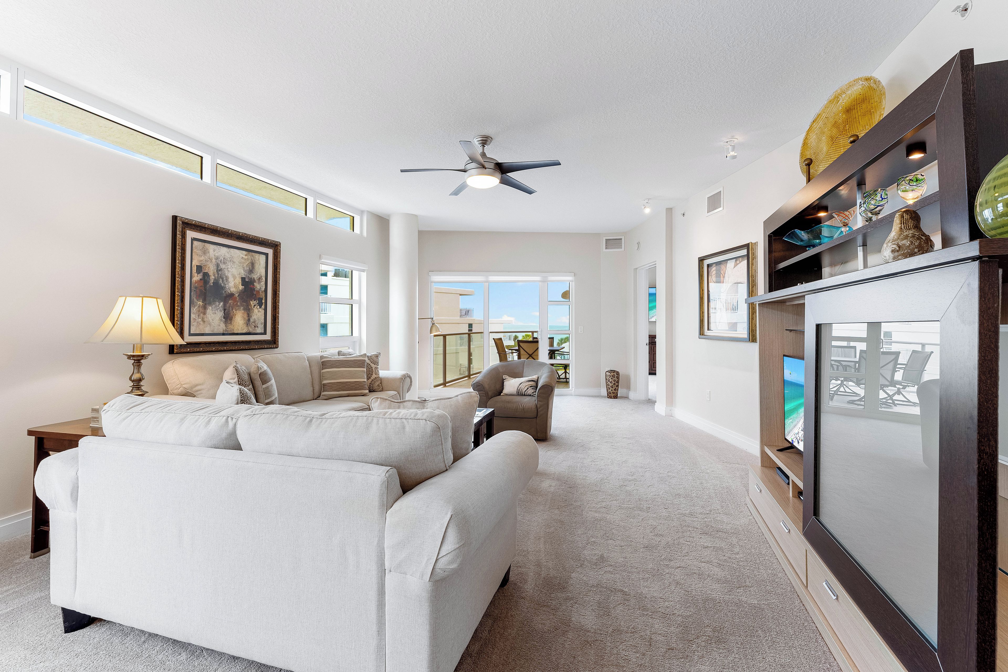 A spacious living room with a large sofa, a television, and a ceiling fan.