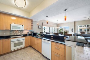 A modern kitchen with wooden cabinets, a built-in microwave, and a large island with a sink. - Crescent Condos by Beachside Management (Siesta Key)