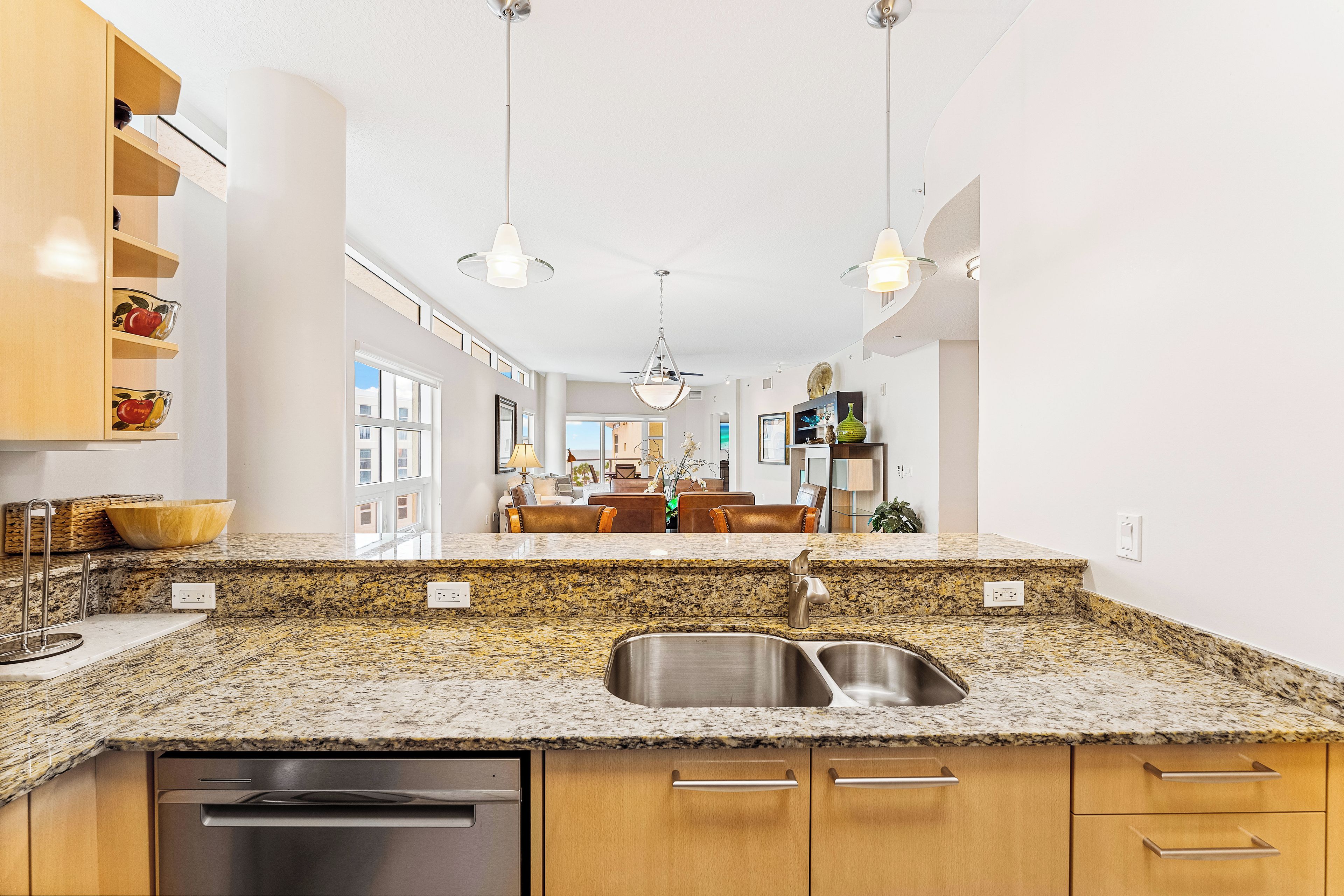 Una cocina moderna con encimeras de granito, pileta de acero inoxidable, muebles de madera e iluminación colgante.