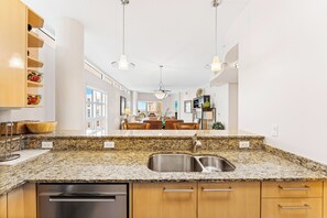 A modern kitchen with granite countertops, stainless steel sink, wooden cabinets, and pendant lighting. - Crescent Condos by Beachside Management (Siesta Key)