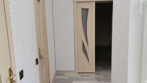 Un pasillo estrecho con suelo de madera, paredes color crema y una puerta con diseño geométrico.
