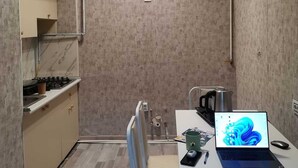 Una cocina compacta con estufa integrada, un lavamanos y una pequeña encimera. Se observa una silla y una mesa con una computadora portátil y un cafetera.