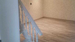 Una habitación amplia con piso de madera, una escalera blanca y un techo inclinado con iluminación empotrada.