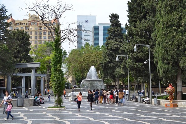 Una plaza pública con una fuente, gente caminando y una estatua.