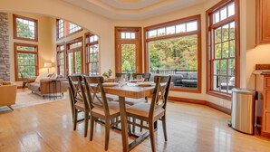 A spacious dining area with a wooden table and chairs, large windows with a view of trees, and a stone accent wall.