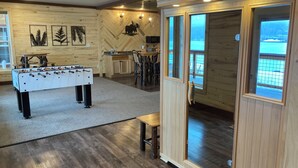 Une pièce chaleureuse avec une table de baby-foot, des murs en bois et une grande fenêtre donnant sur un paysage enneigé.