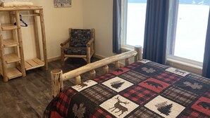 Una habitación acogedora con una cama de madera, una silla, una escalera y un ventanal con vistas a un paisaje nevado.