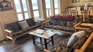 Una habitación acogedora de estilo cabaña, con dos sofás estampados, una mesa de centro y una mesa de comedor con sillas.