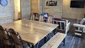 Un interior de madera con una gran mesa de comedor, bancos y un reloj fijado en la pared.