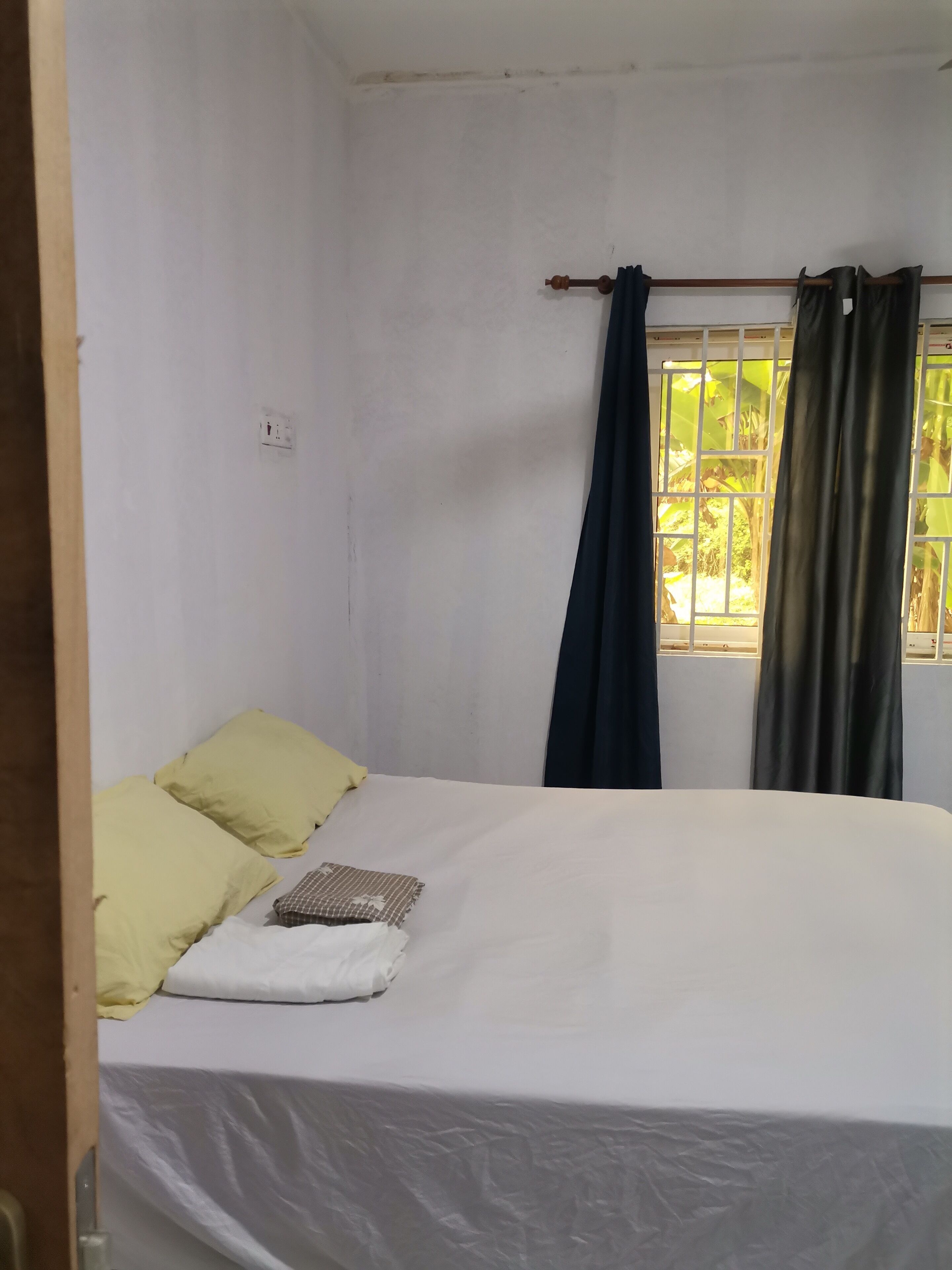 Una habitación pequeña y sencilla con una cama, una ventana con cortinas y un enchufe a la vista.