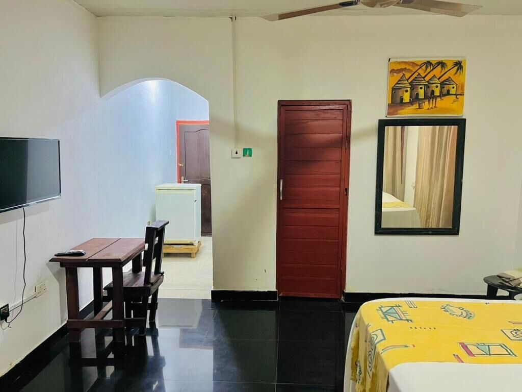 Habitación de hotel con cama, escritorio, silla, televisión, puerta roja y un cuadro en la pared.