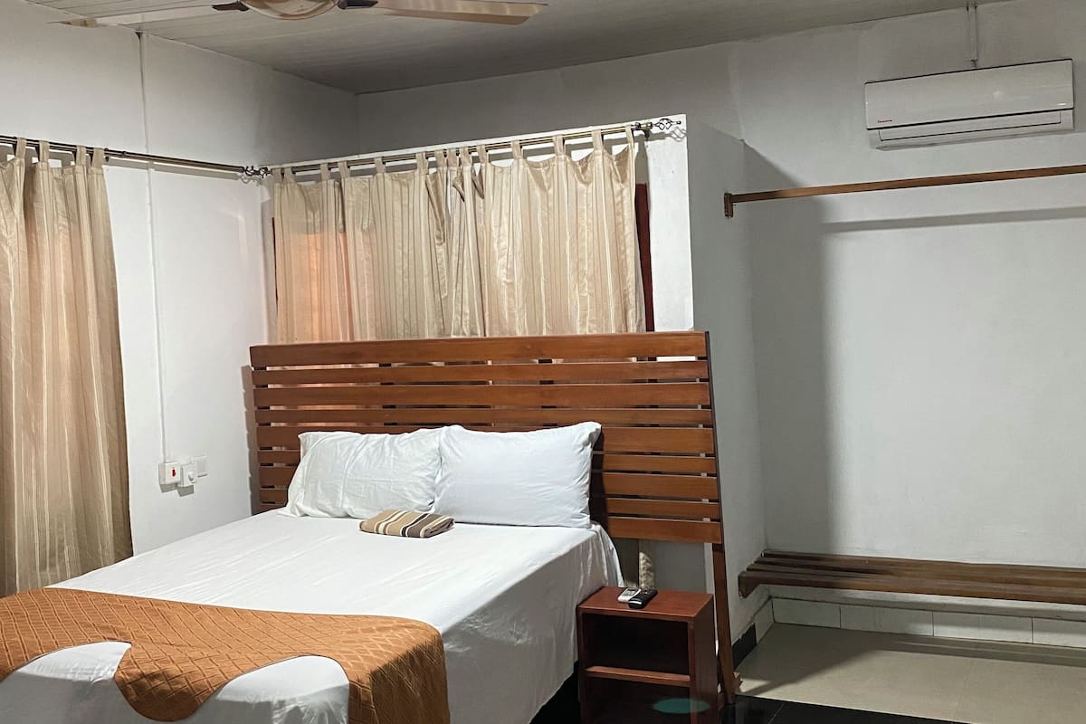 Een slaapkamer met een houten bed, een nachtkastje, een plafondventilator en een airconditioner.