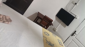 Een kamer met een bed, een houten stoel, een aan de muur bevestigde televisie en een deur.