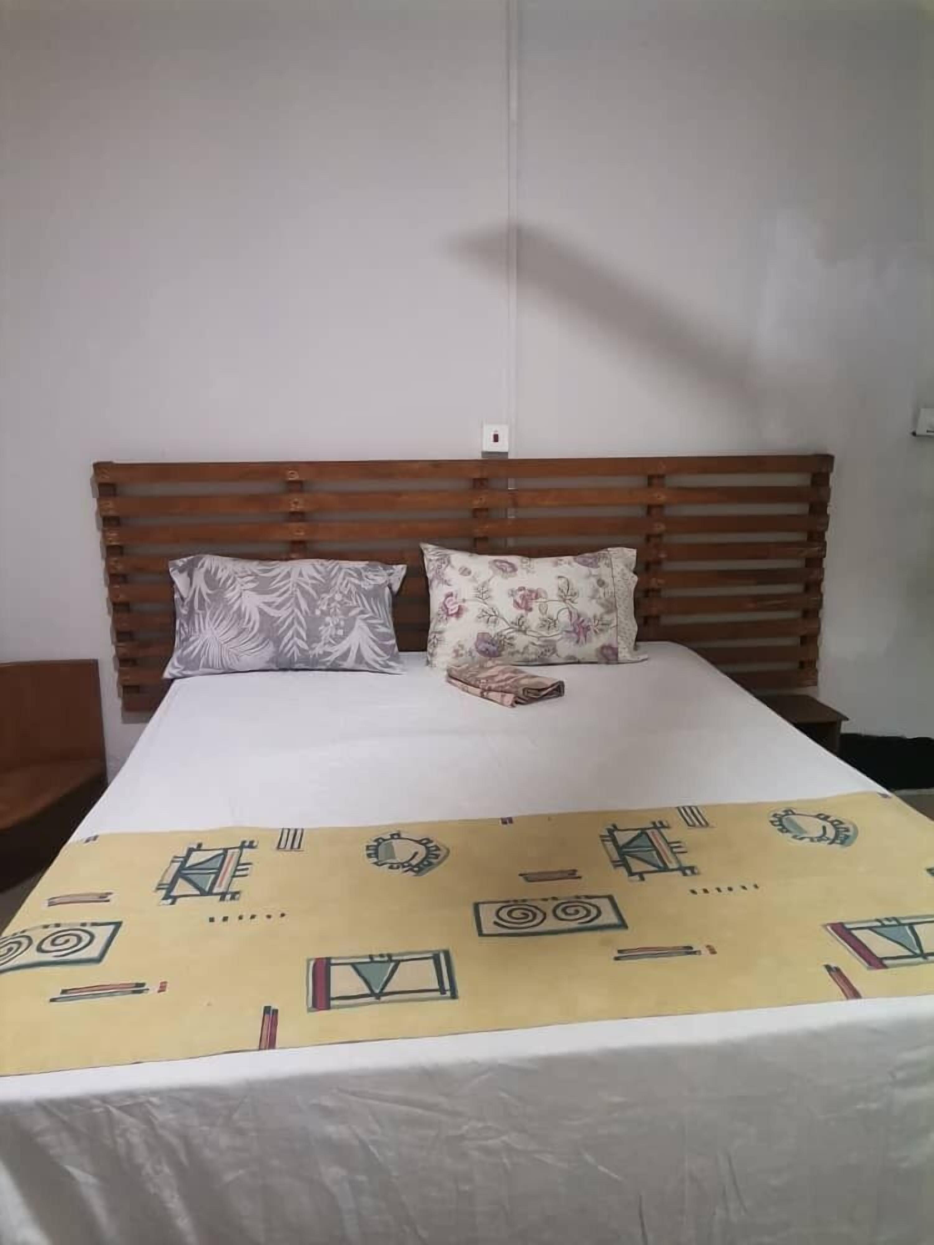 Una cama con cabecera de madera, dos almohadas y una colcha estampada.