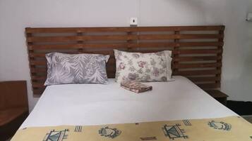 Una cama con cabecera de madera, dos almohadas y una colcha estampada.