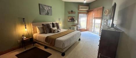 Um quarto com cama, mesas de cabeceira, cômoda, janela com persianas e luminária de teto.
