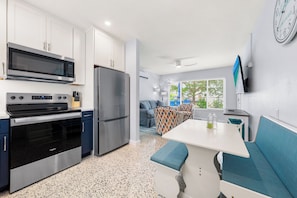 A modern kitchen with stainless steel appliances, a dining area with a bench, and a view of greenery outside. - Hidden Paradise by Beachside Management (Siesta Key)