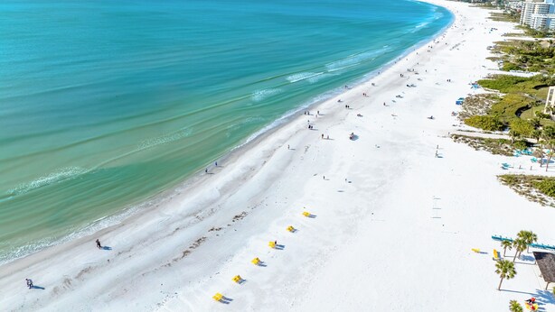 A wide beach with clear blue water, a long stretch of white sand, and a few people walking. - Hidden Paradise by Beachside Management (Siesta Key)