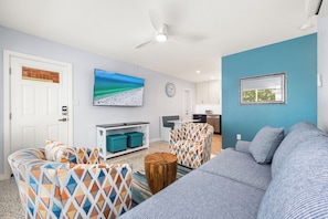 A living room with a sofa, patterned armchairs, a coffee table, a TV, a clock, and a framed picture on the wall. - Hidden Paradise by Beachside Management (Siesta Key)
