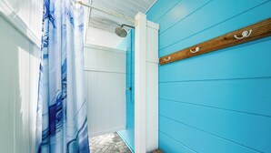 A bathroom with a blue wall, a wooden bench, a shower curtain, and a wooden shelf with hooks. - Hidden Paradise by Beachside Management (Siesta Key)