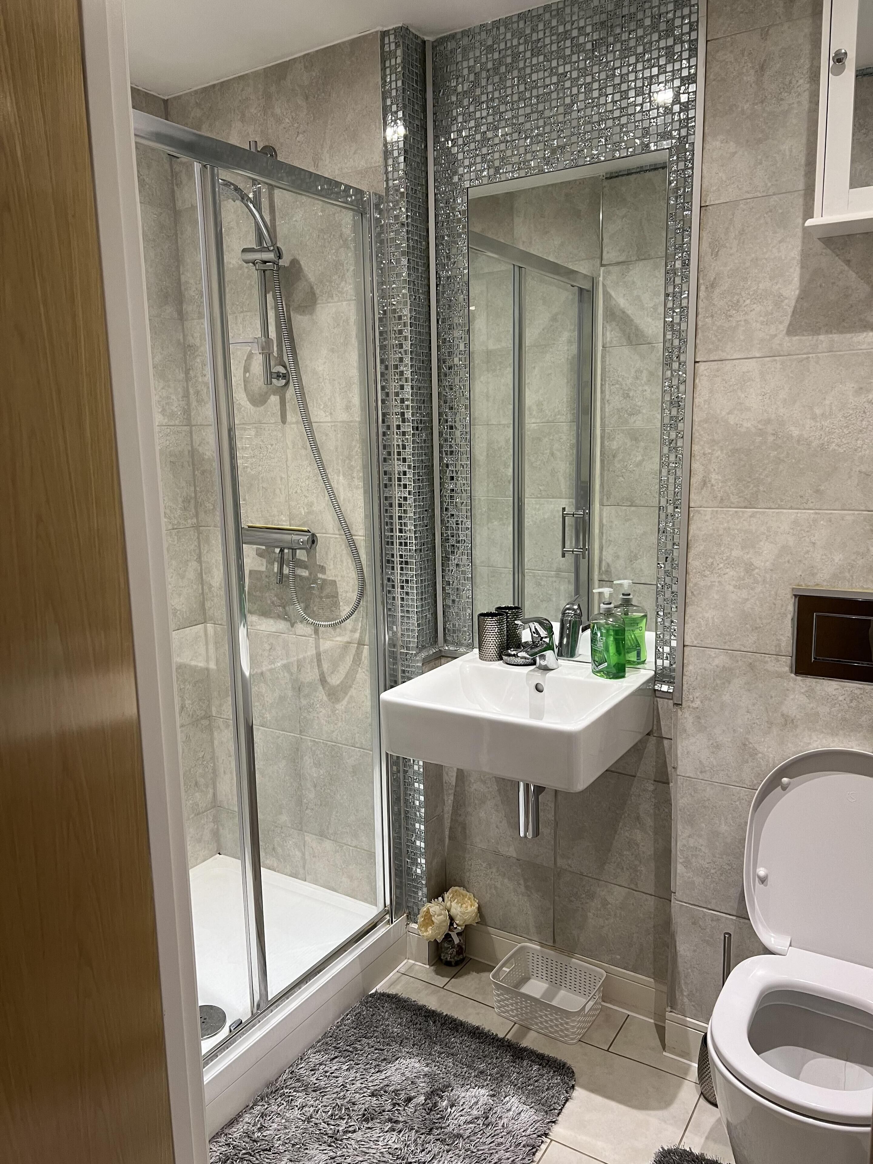 Un baño moderno con cabina de ducha de vidrio, un lavabo blanco con artículos de aseo y un inodoro.