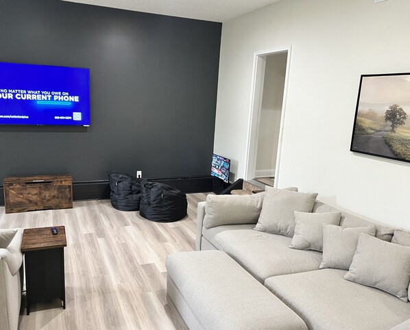 Ein modernes Wohnzimmer mit einem grauen Sofa, schwarzen Sitzsäcken, einem Holztisch und einem flachbildfernseher an der Wand.