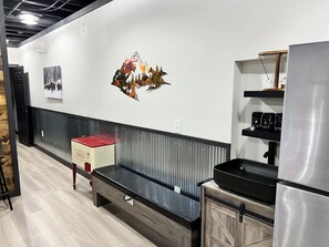 A modern kitchen with a stainless steel refrigerator, a built-in oven, and a coffee machine on a black countertop.